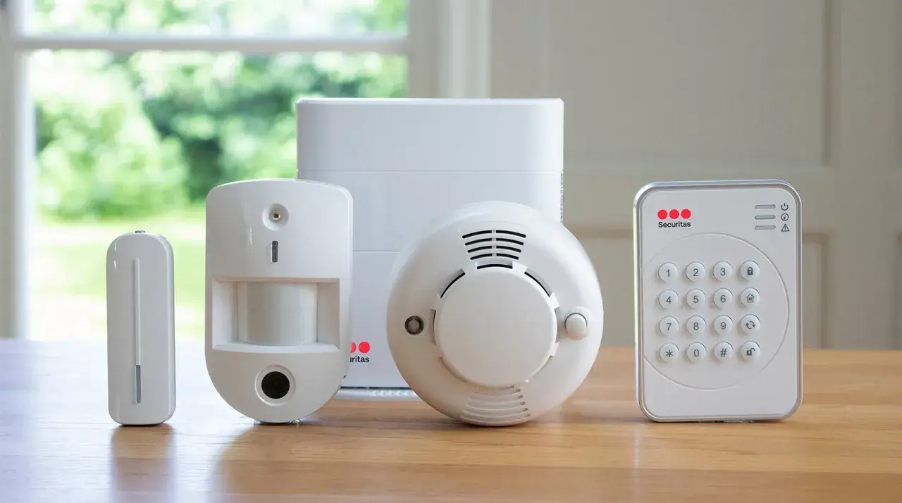 En uppsättning säkerhetskomponenter: en rörelsedetektor, en dörr-/fönstersensor, en rökdetektor och ett kontrollpanel med knappsats. Allt redo för att ge en alert alarm.