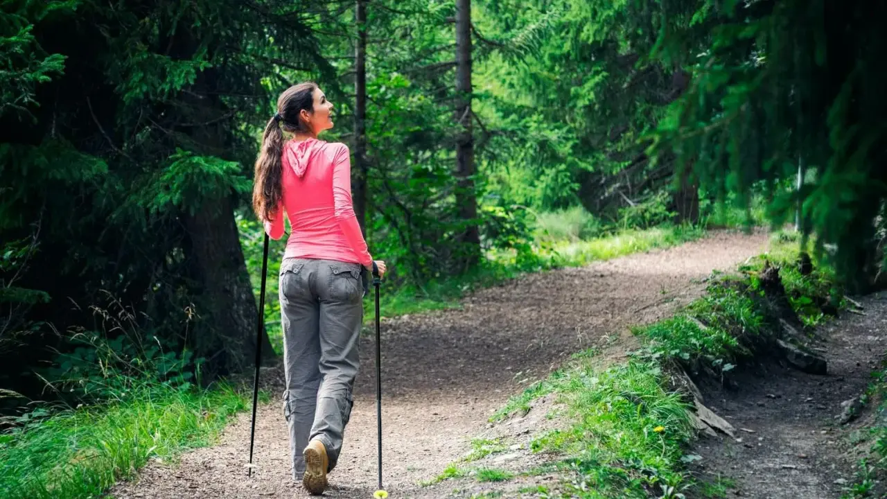 Kvinna går med stavar på en grusväg i en grönskande skog.