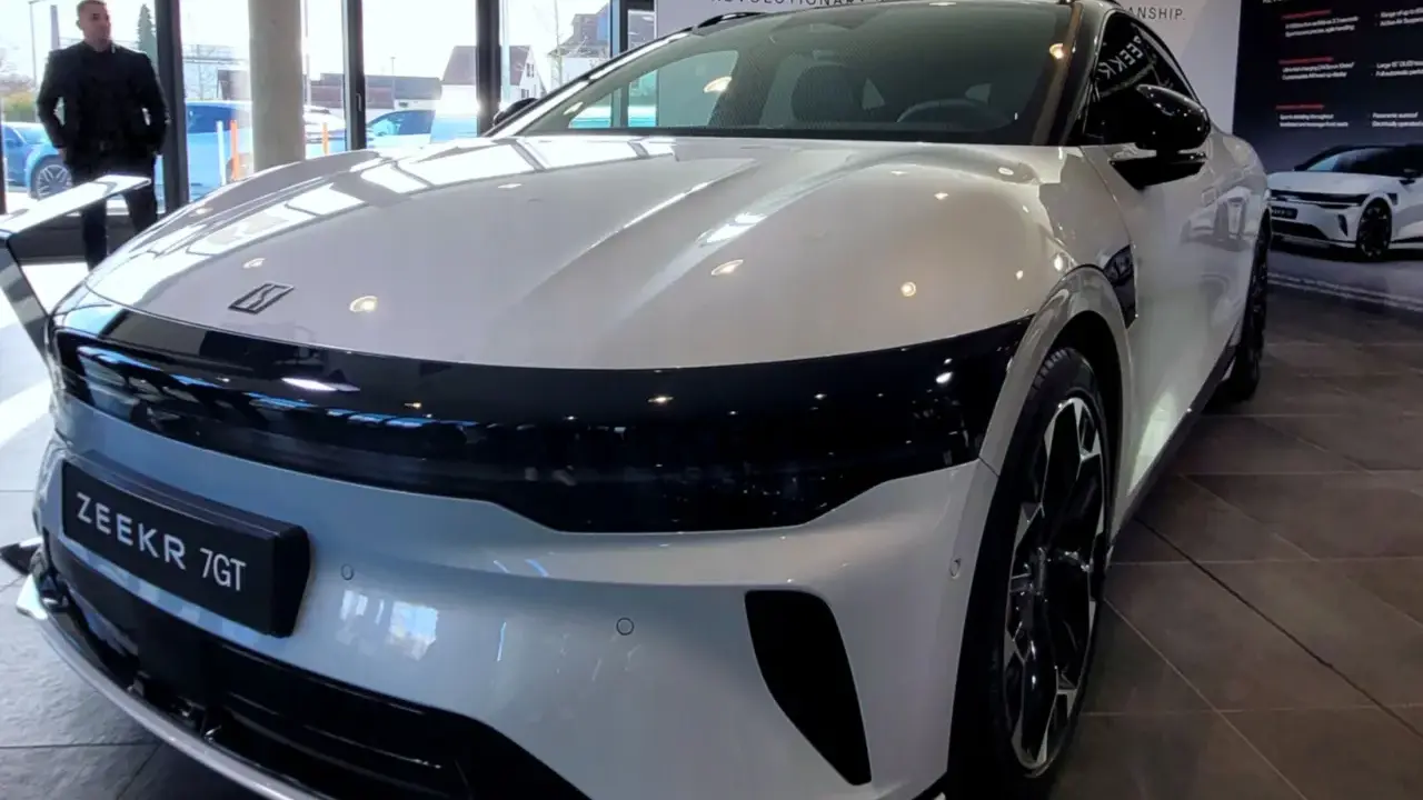 Ein Mann steht vor einem glänzenden, weißen Zeekr 7 GT in einem Ausstellungsraum. Das Auto hat eine markante schwarze Frontpartie.