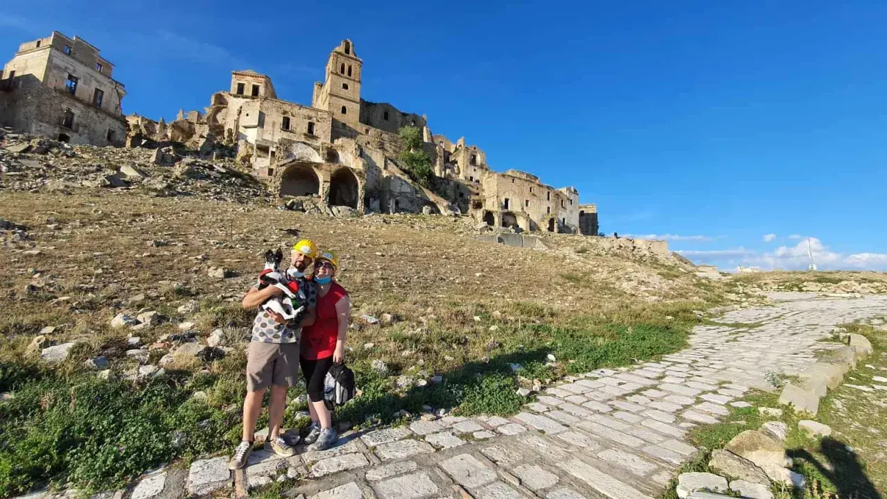 Coppia con cane visita le suggestive rovine di Craco vecchia, un borgo fantasma sotto un cielo azzurro.