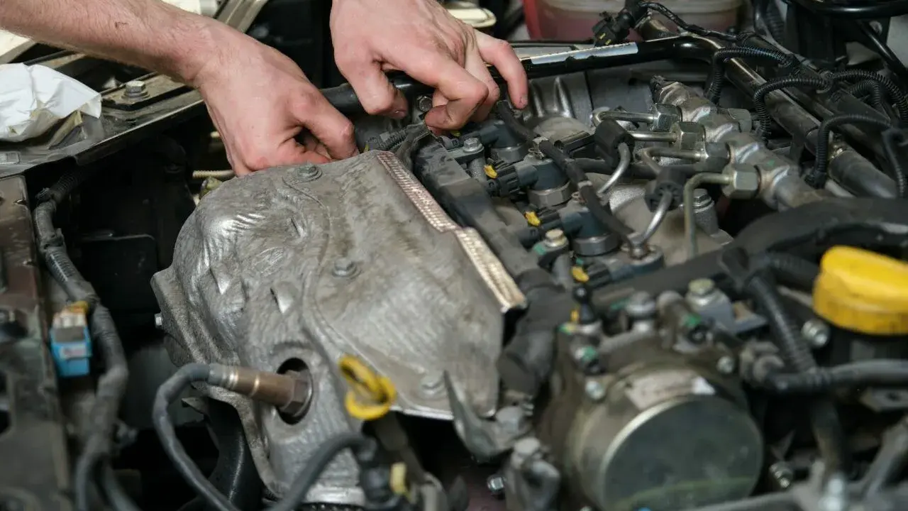 Mechanik pracuje przy silniku, sprawdzając czujnik wałka rozrządu. Objawy jego awarii mogą być różne.