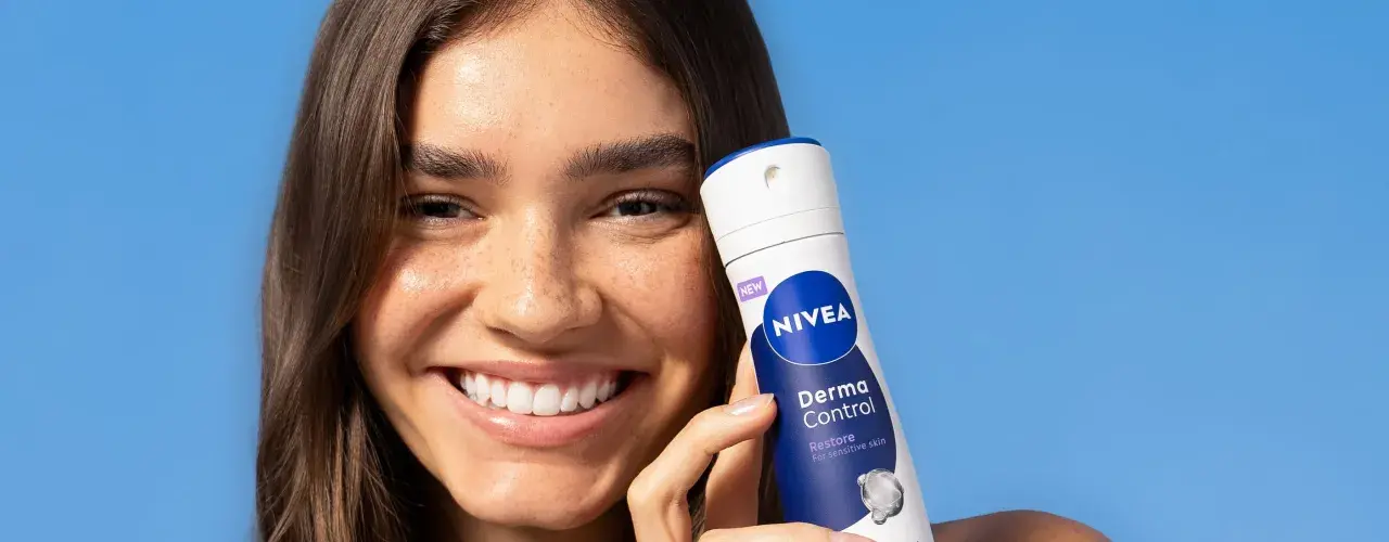 Donna sorridente con prodotto Nivea Derma Control, ideale per chi soffre di bruciore sotto le ascelle.