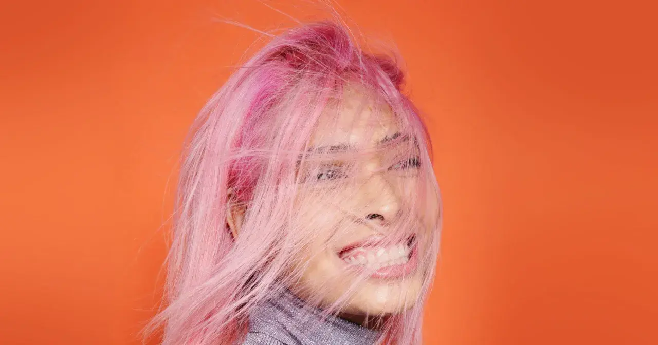 Frauenkopf mit pinken Haaren, die im Wind wehen. Ein Antistatik-Spray für Haare hätte hier Wunder gewirkt.