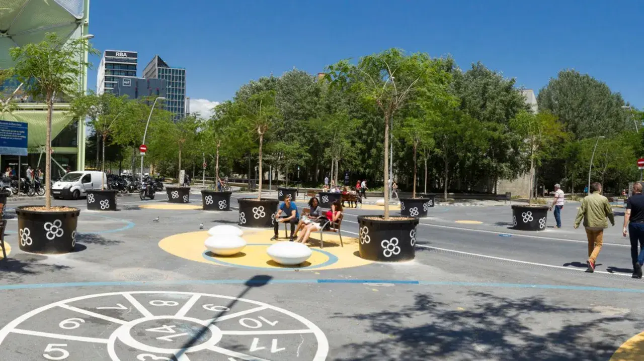 Barcelona autofrei: Menschen genießen einen grünen Platz mit Bäumen in großen Kübeln, Sitzgelegenheiten und einem Spielbereich auf dem Boden.