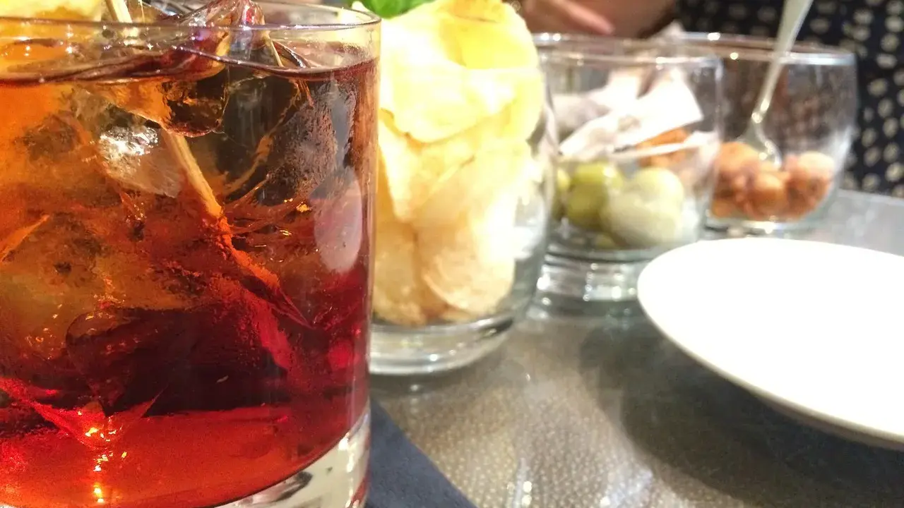 Czerwony drink z lodem i cytryną, obok chipsy i oliwki. Idealny aperitif, jak zrobic martini?
