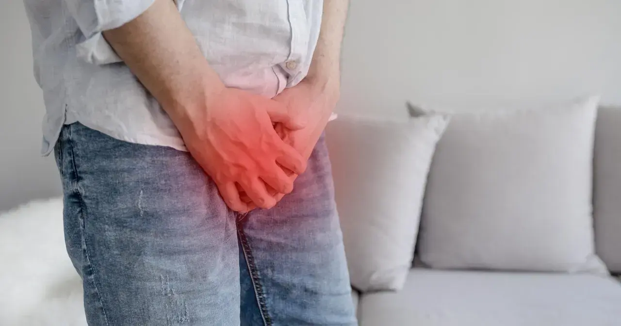 Mężczyzna trzyma się za krocze, gdzie widoczny jest czerwony obszar bólu, sugerujący chorobę Peyroniego.