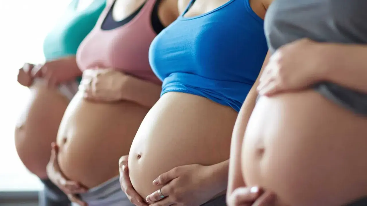 Fyra gravida kvinnor står sida vid sida och håller sina magar. En av dem, andfådd gravid, ler.