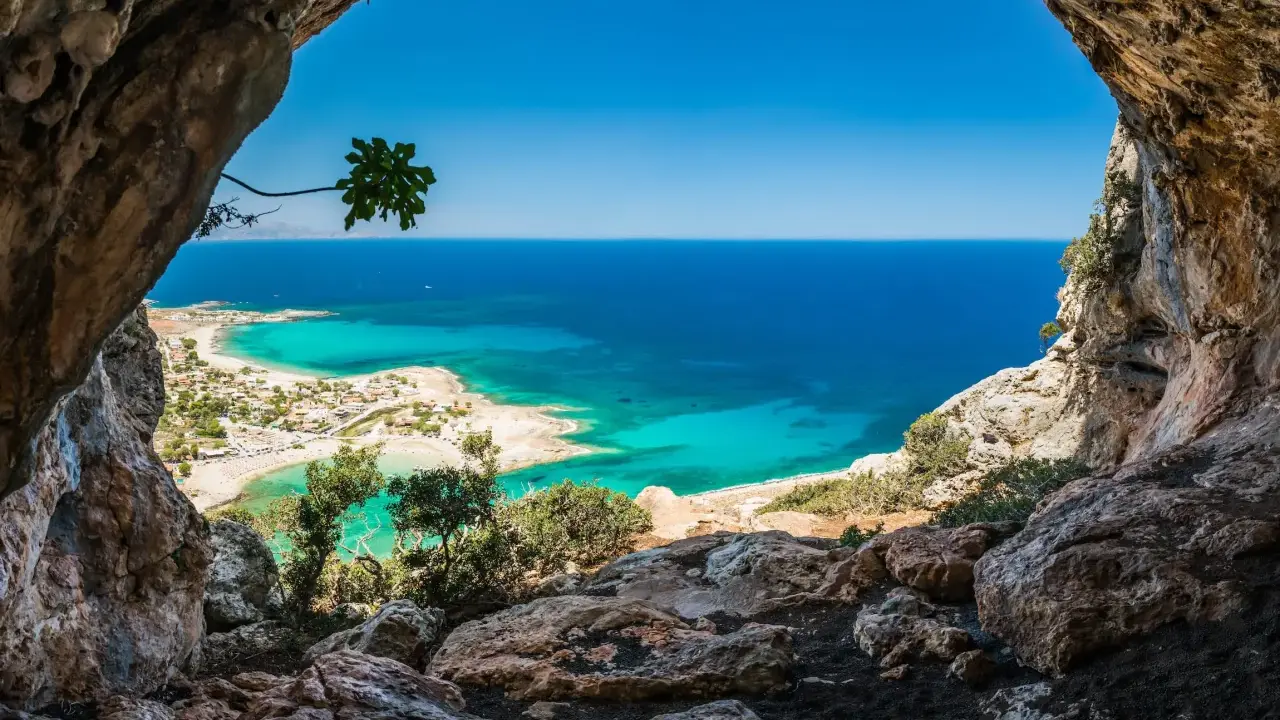 Widok z jaskini na turkusowe morze i plażę. Idealna kreta pogoda w kwietniu, słońce i błękitne niebo.