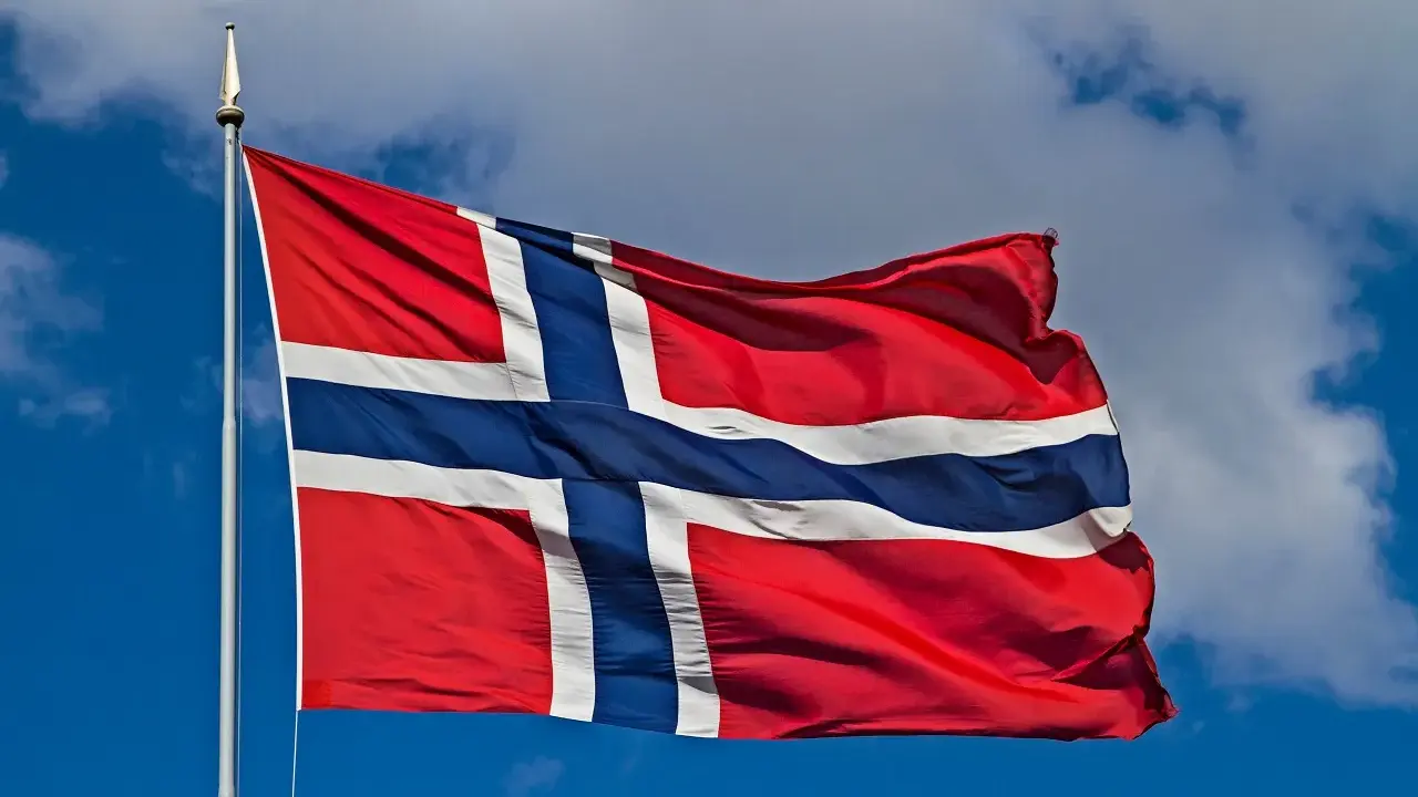 Norweska flaga powiewa na wietrze. W tle błękitne niebo z chmurami. Takie są prace, gdy jest piękna pogoda.