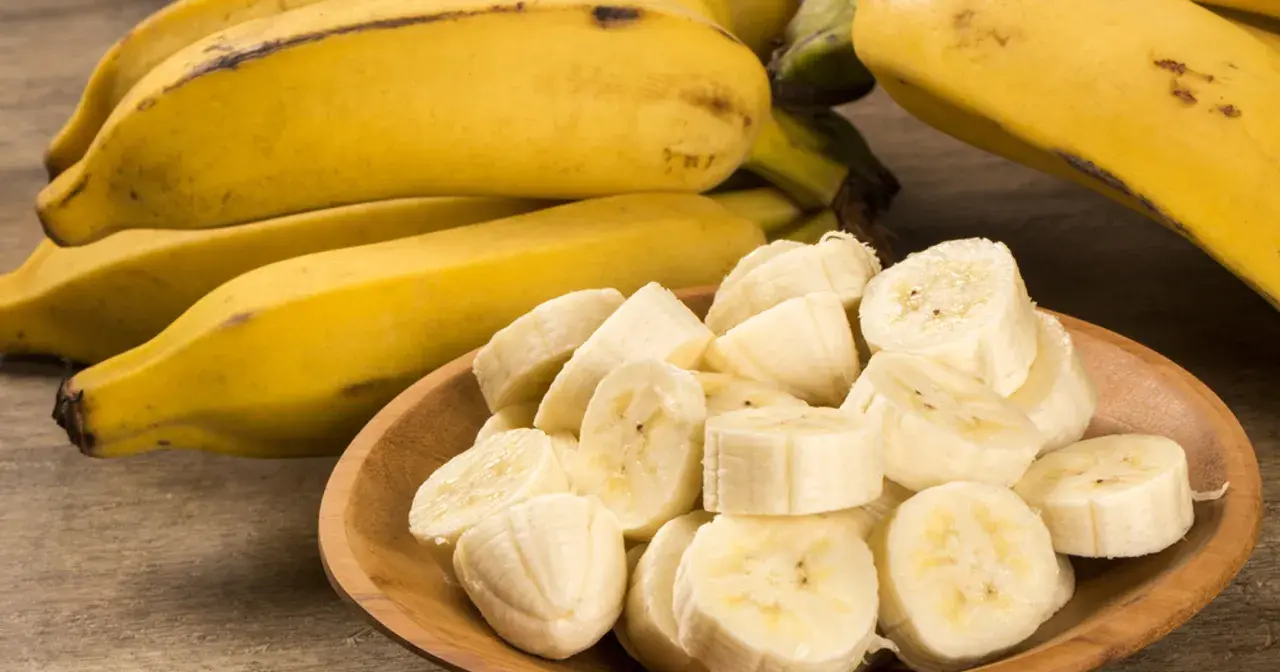 Kawałki bananów w drewnianej misce obok całych owoców. Te żółte banany, bogate w potas, są świetne dla zdrowia nerek.