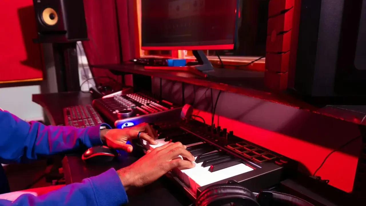 Les mains d'une personne jouent sur un clavier, entourées d'équipement de studio, un rêve de devenir beatmaker.