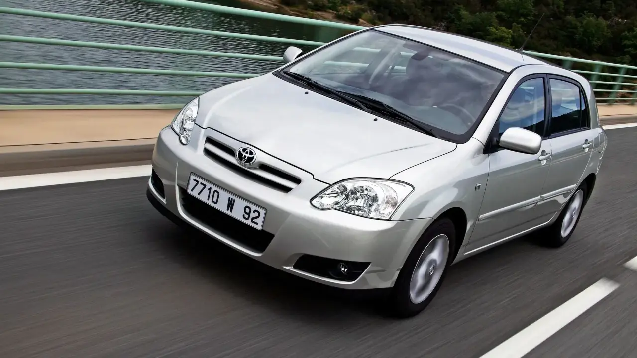 Srebrna Toyota Corolla 2004 na moście, z widokiem na wodę i las.