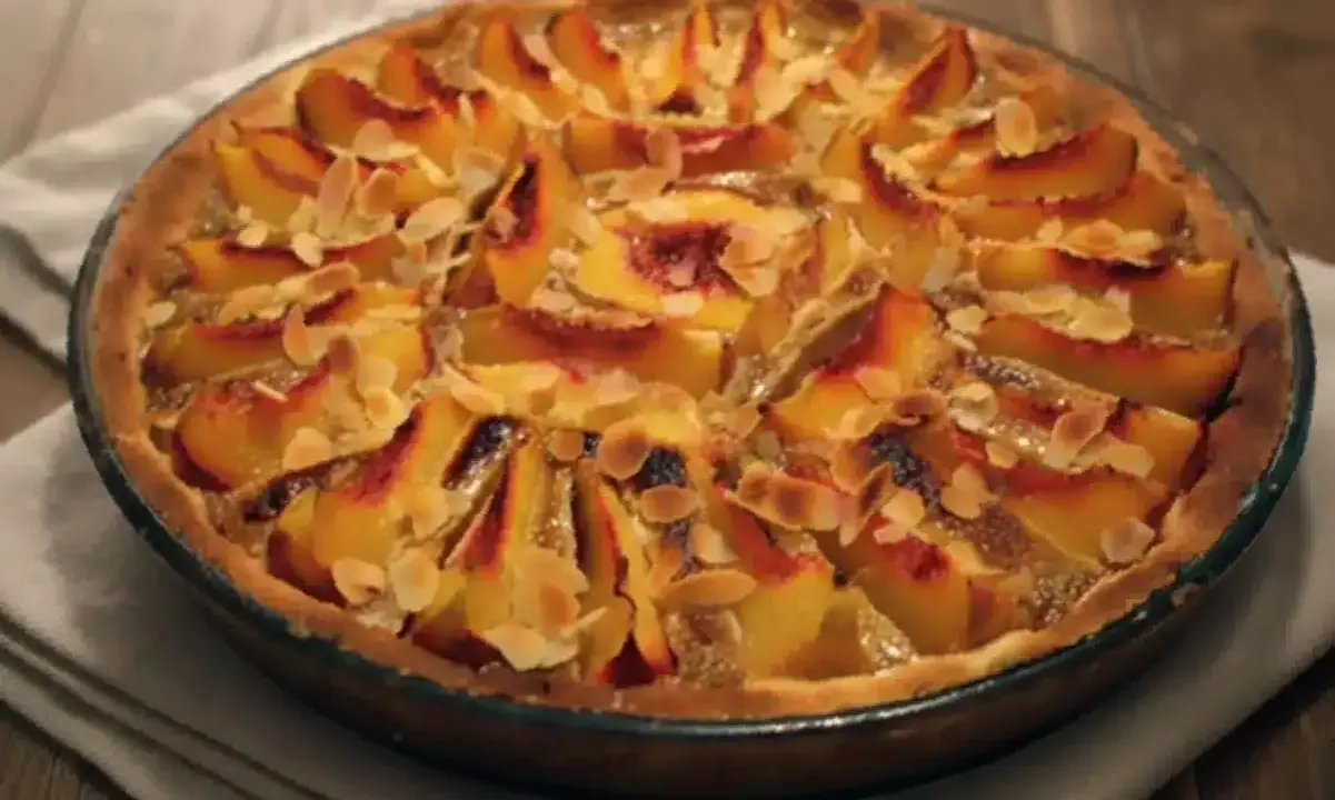 Tarte aux pêches amande, une gourmandise dorée aux fruits fondants et éclats d'amandes effilées, prête à être dégustée.