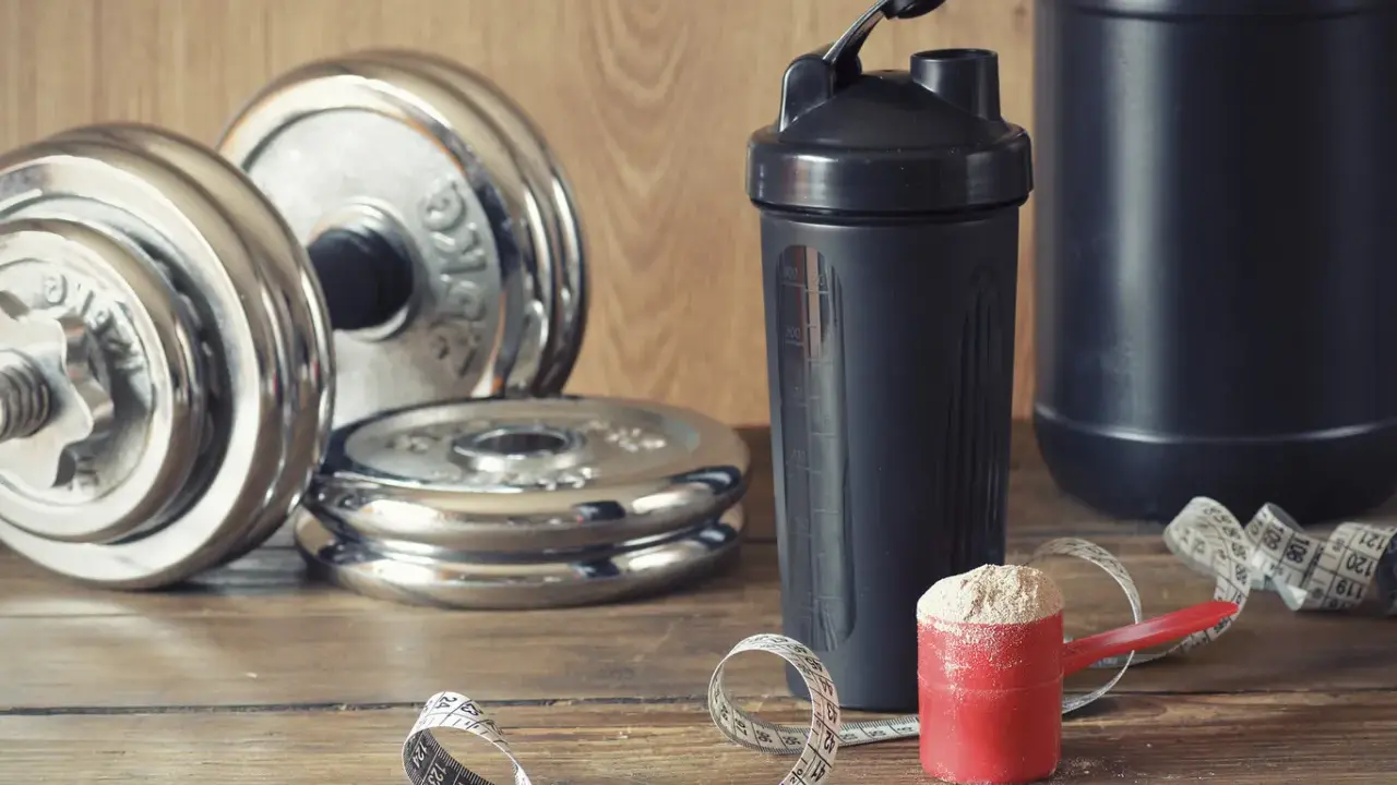 Pesas, batidora y cuchara con proteína en polvo. Ideal para saber cuándo tomar batido de proteínas y optimizar tu entrenamiento.