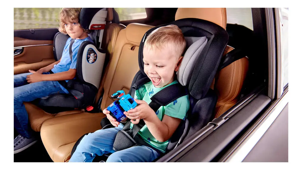 Uśmiechnięty chłopiec bawi się zabawką w foteliku Kinderkraft Comfort Up ADAC. Obok siedzi starszy brat.