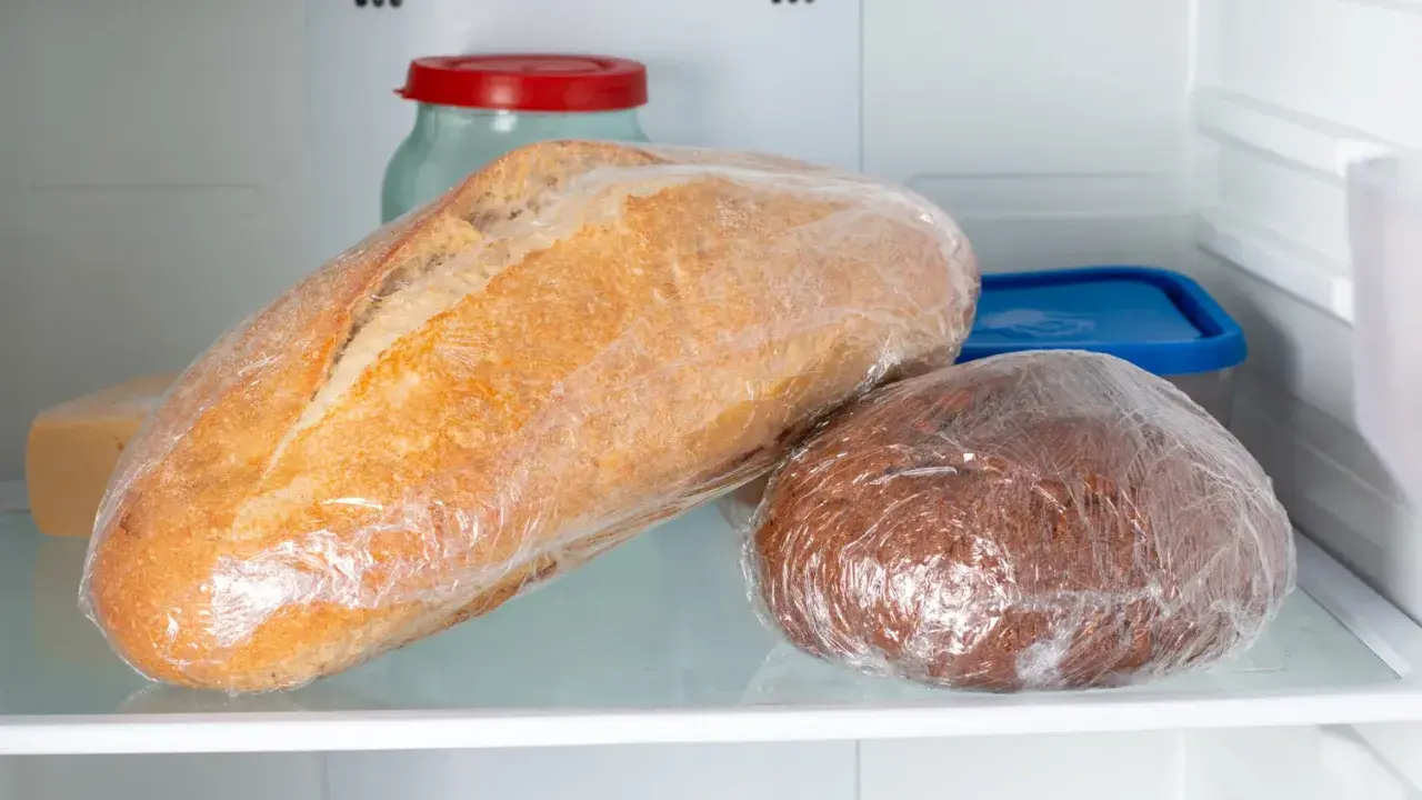 Deux pains emballés dans du film plastique, un pain blanc et un pain brun, sont rangés dans le frigo.