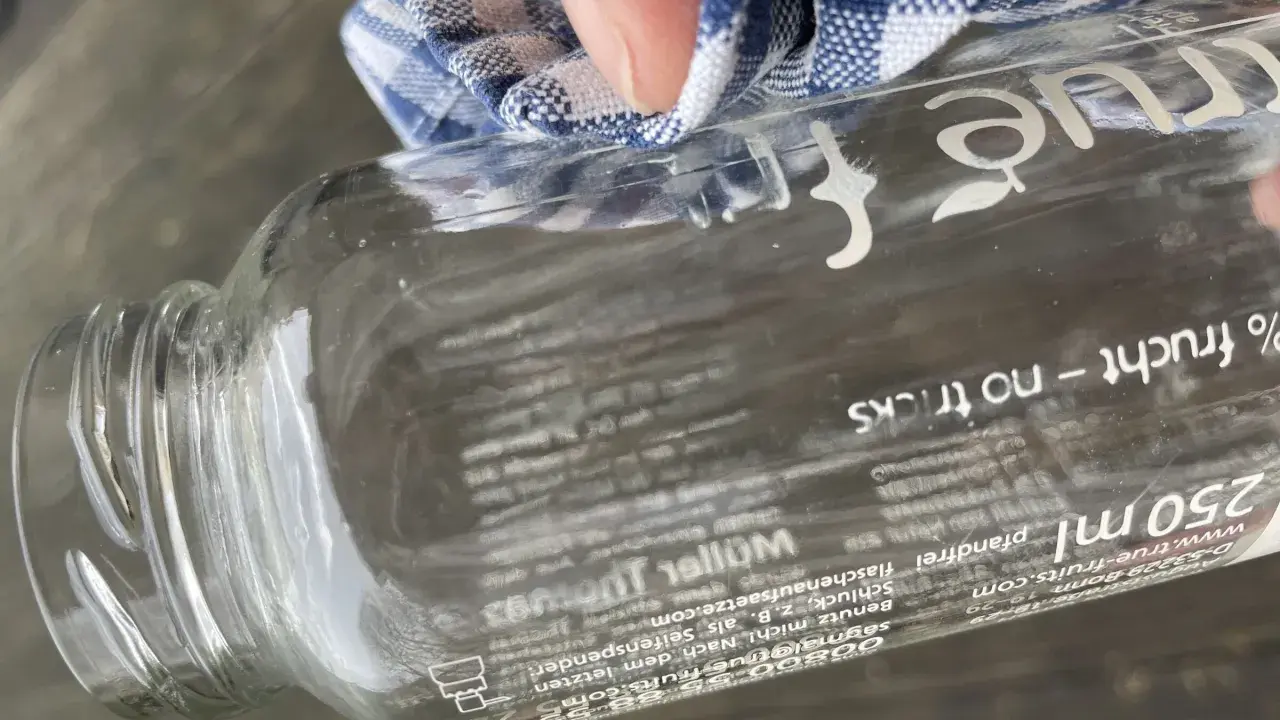 Mit einem Tuch wird das "true fruits" Schrift entfernt. Die Flasche ist aus Glas und hat einen Pfandaufdruck.