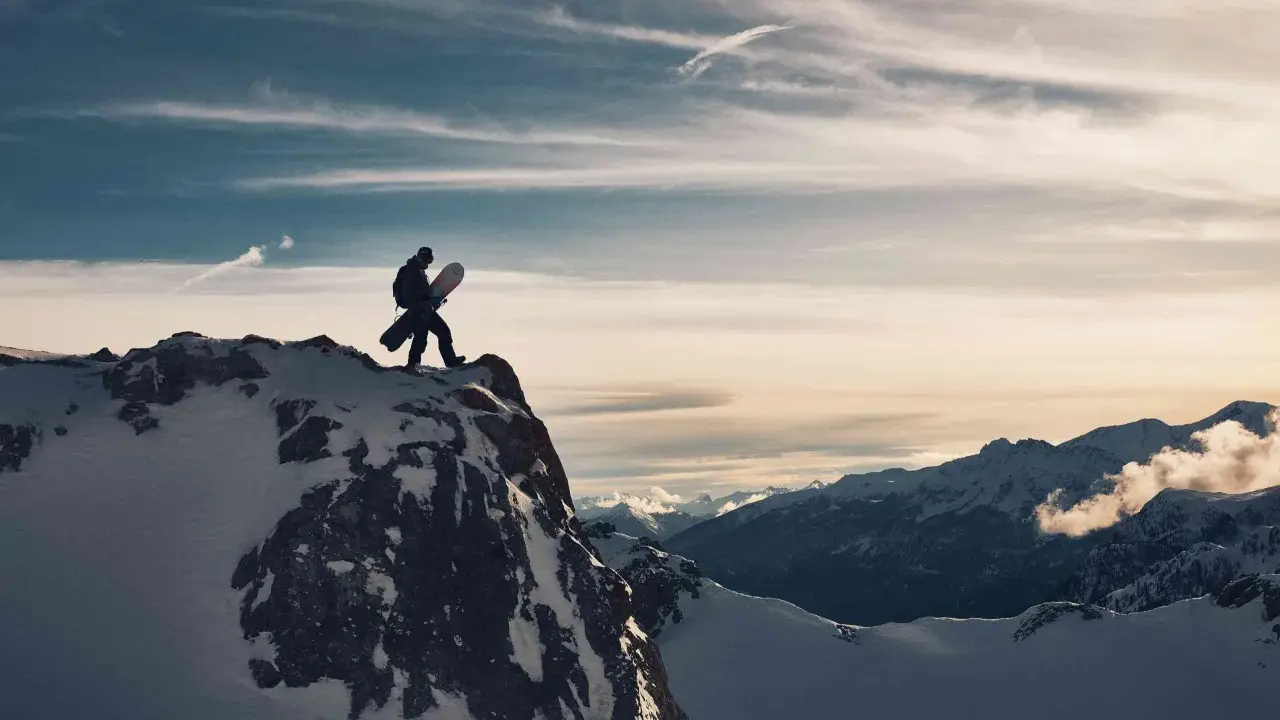 Sylwester w Alpach: snowboardzista na szczycie góry, gotowy na zjazd. W tle majestatyczne, ośnieżone szczyty i dramatyczne chmury.