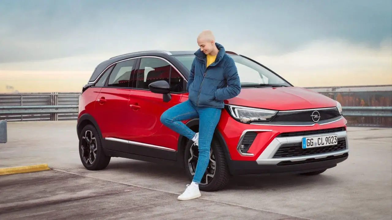 Joven apoyada en un Opel Crossland X rojo. Evita problemas con la correa de distribución de tu Opel Crossland X con un mantenimiento adecuado.