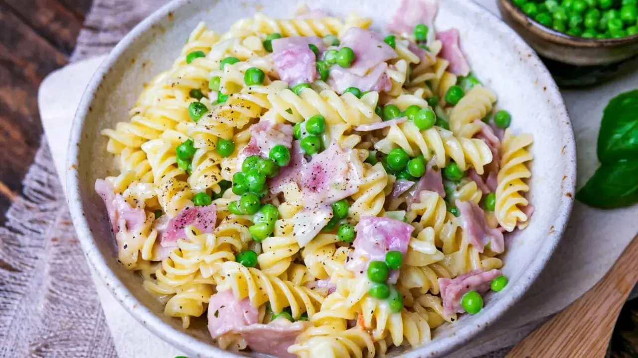 Fusilli-Nudeln mit Erbsen und Schinken in einer cremigen schinken sahne sauce, bestreut mit schwarzem Pfeffer.