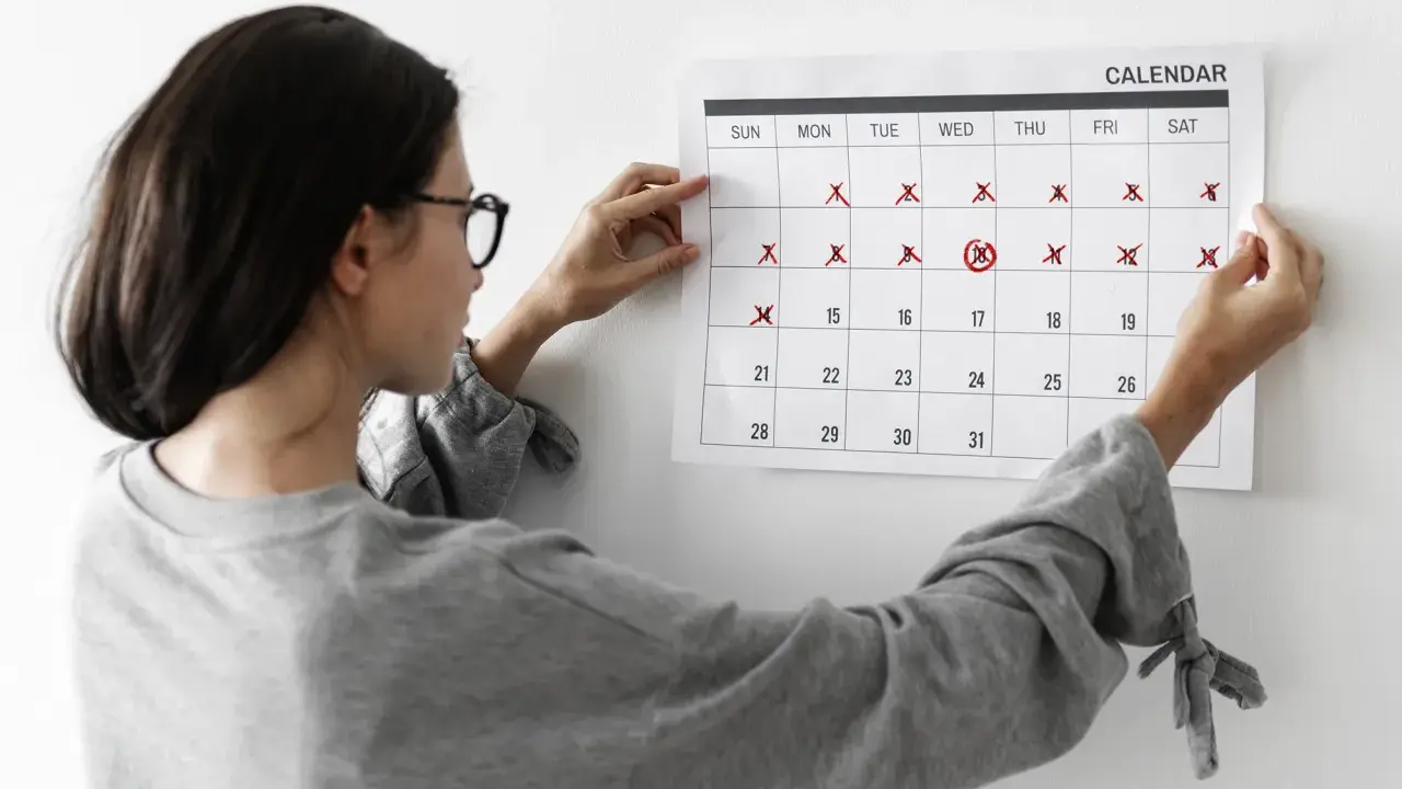 Mujer revisa calendario, marcando días. No me baja la regla y no estoy embarazada, preocupación en su rostro.