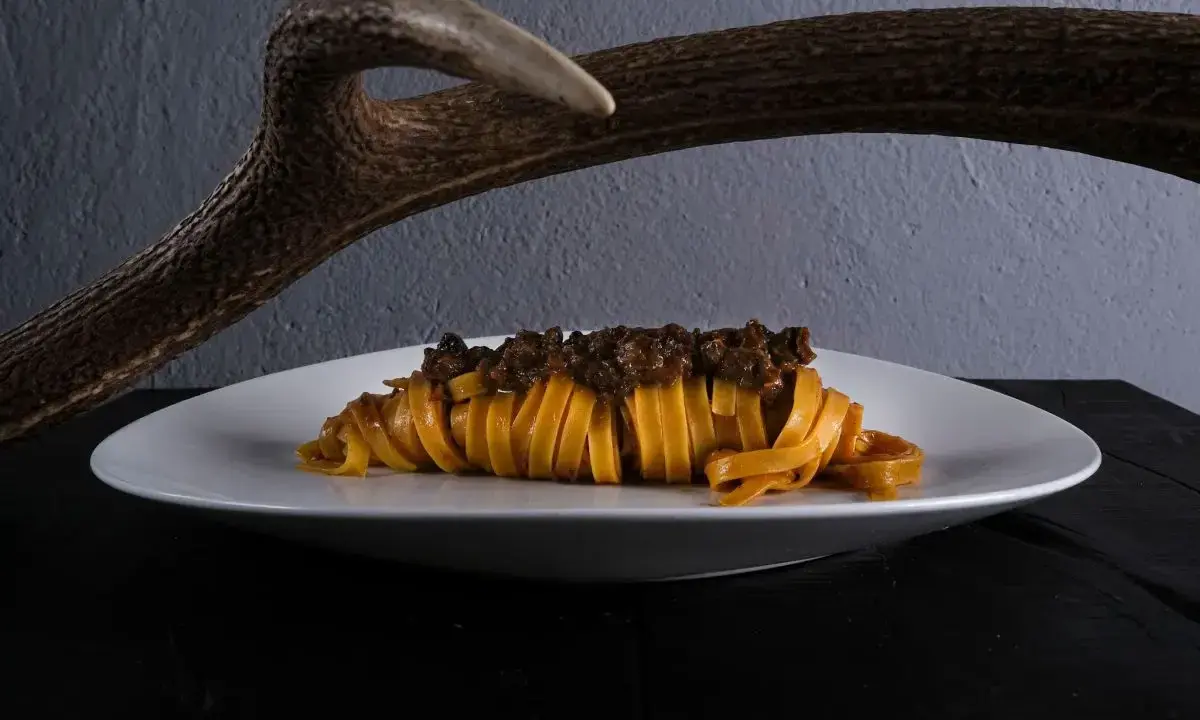 Un piatto di pasta fresca con ragù di cinghiale, un'autentica esperienza di mangiare toscano, con un palco di cervo sullo sfondo.