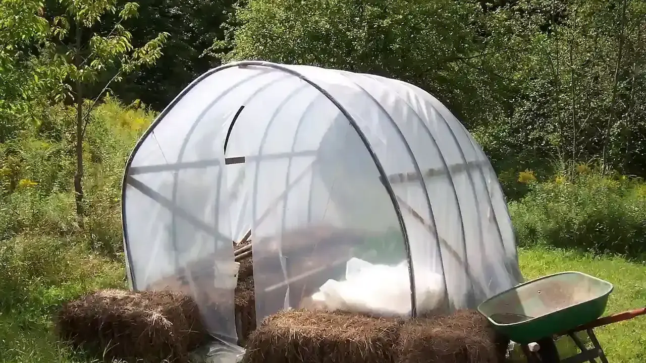 Un invernadero listo para el huerto de verano, con fardos de paja y carretilla a los lados.
