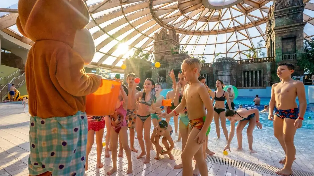Maskotka rzuca piłeczki dzieciom w aquaparku w Budapeszcie. Radosna zabawa pod szklaną kopułą.