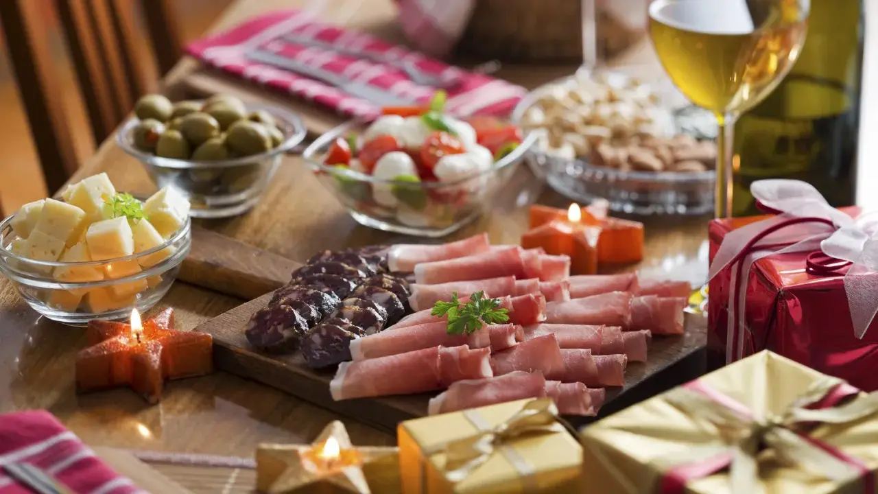 Eleganckie menu na sylwestra w domu: wędliny, sery, oliwki, pomidorki z mozzarellą, orzechy, wino i prezenty.