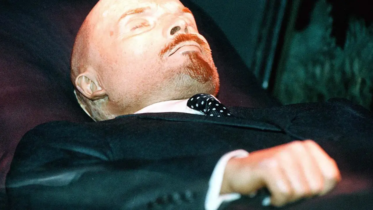 Mumia Lenina w garniturze i z krawatem w kropki, spoczywająca w szklanej gablocie.