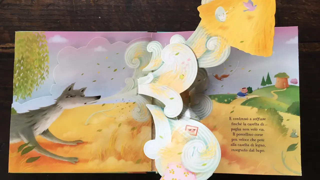 Libri pop-up più belli: un lupo soffia su una casetta di paglia, mentre un maialino corre verso una casetta di legno.