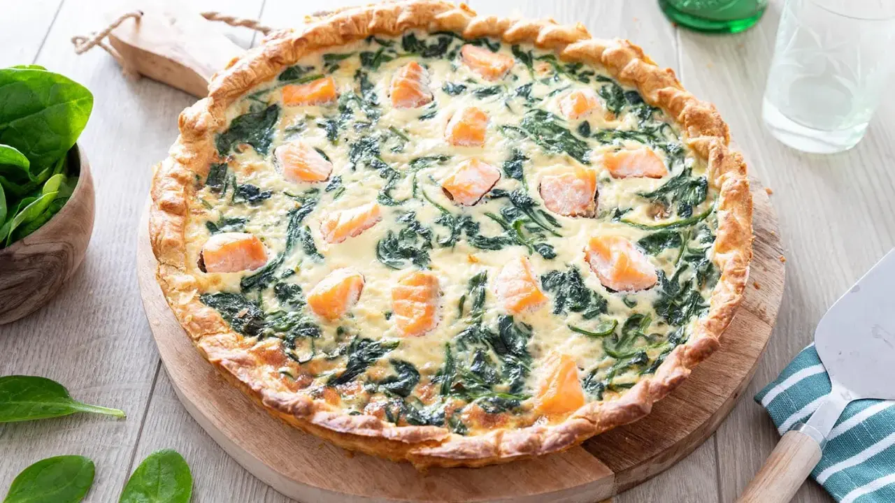 Une délicieuse quiche saumon épinard, dorée et garnie de morceaux de poisson et de légumes verts, prête à être dégustée.