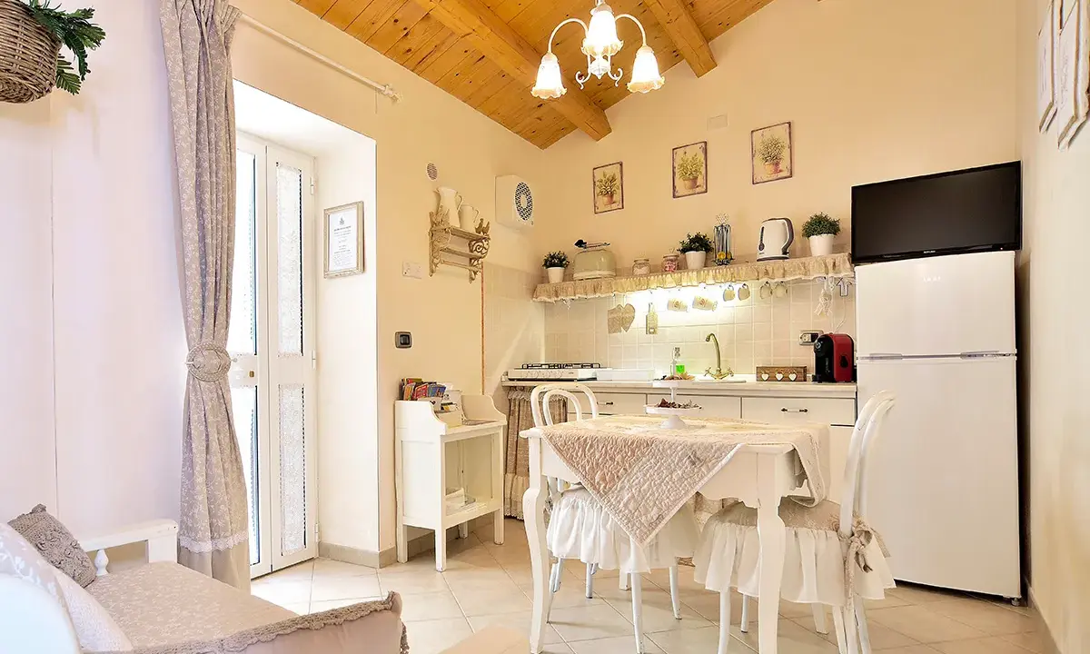 Cuisine et coin repas dans un style shabby chic, avec des meubles blancs, des textiles doux et des poutres apparentes.