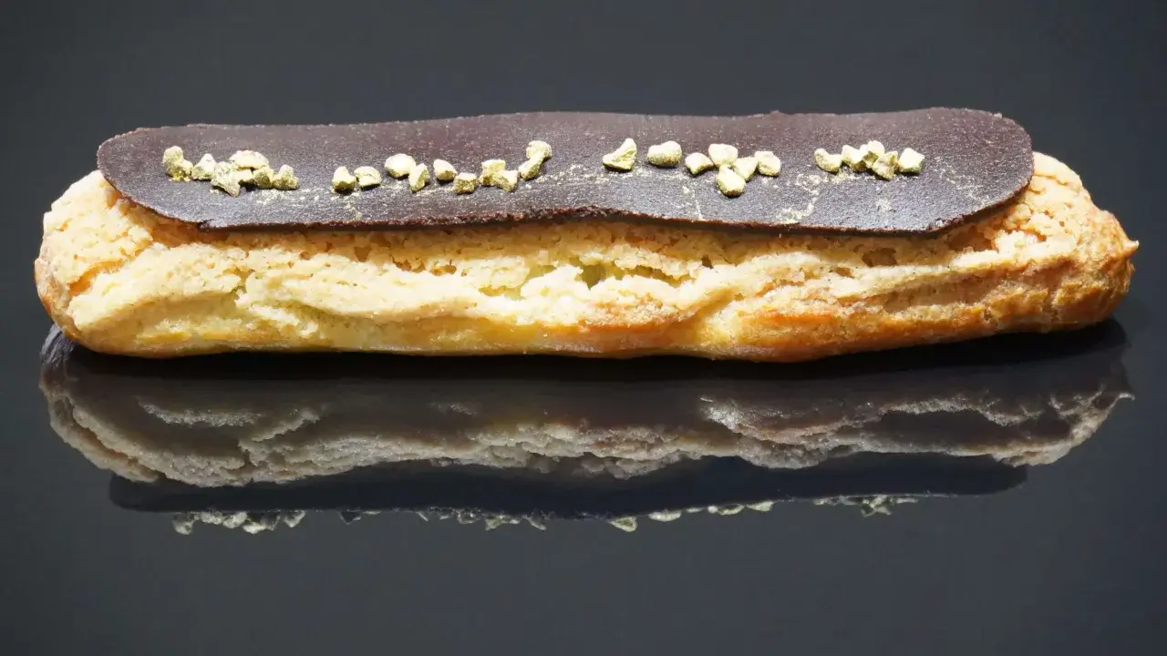 Un délicieux éclair au chocolat, garni de petits éclats dorés, repose sur une surface réfléchissante.