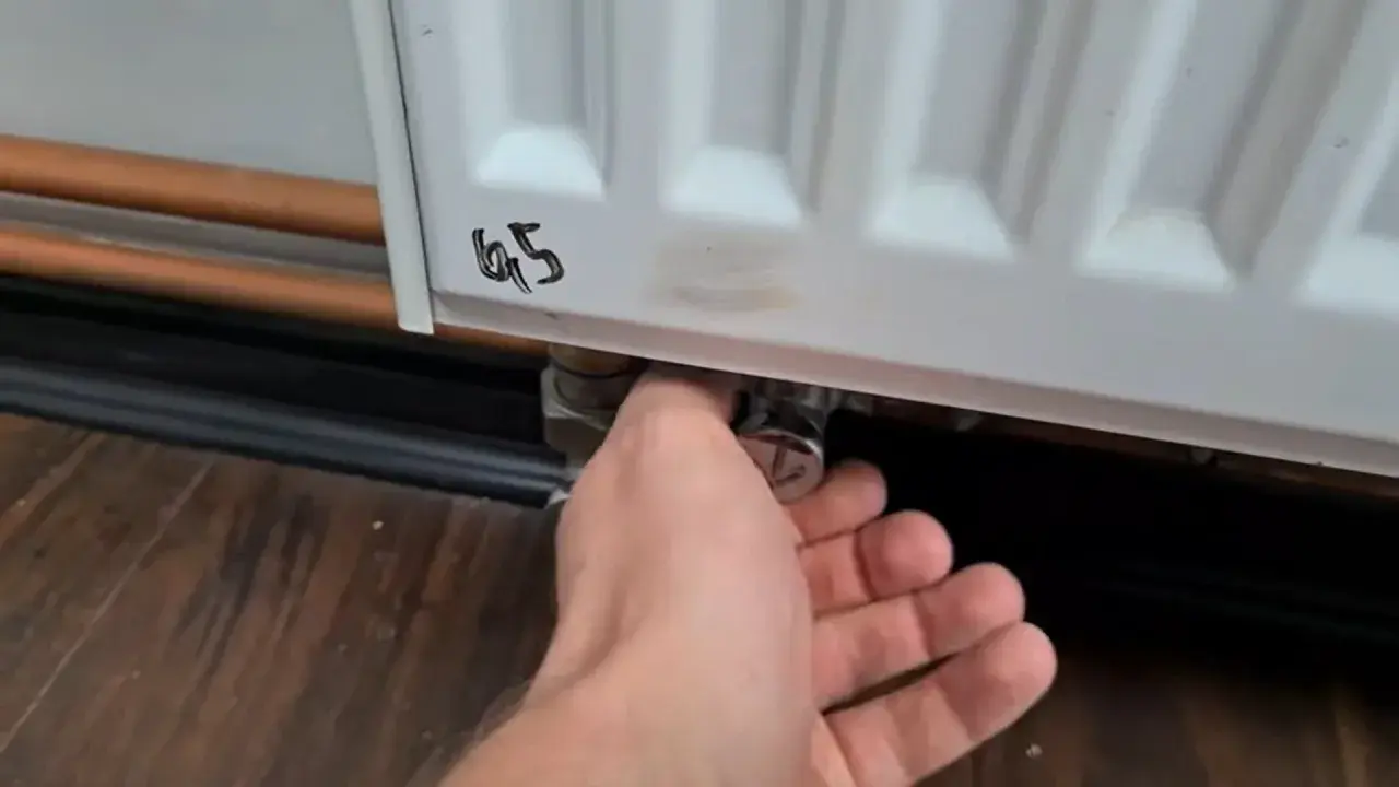 Ręka reguluje zawór grzejnika aluminiowego, próbując wyeliminować szum w grzejnikach aluminiowych.