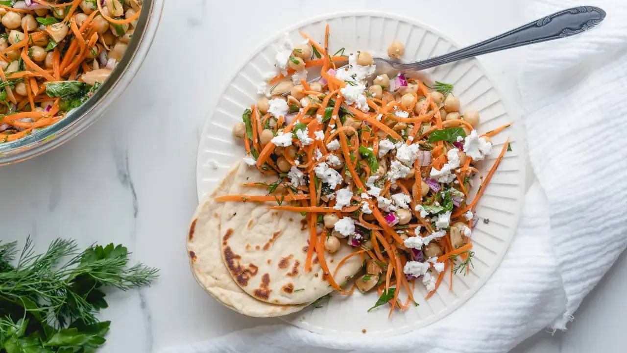 Salade de pois chiches et carottes râpées assaisonnement frais, garnie de feta émiettée et servie avec du pain plat.