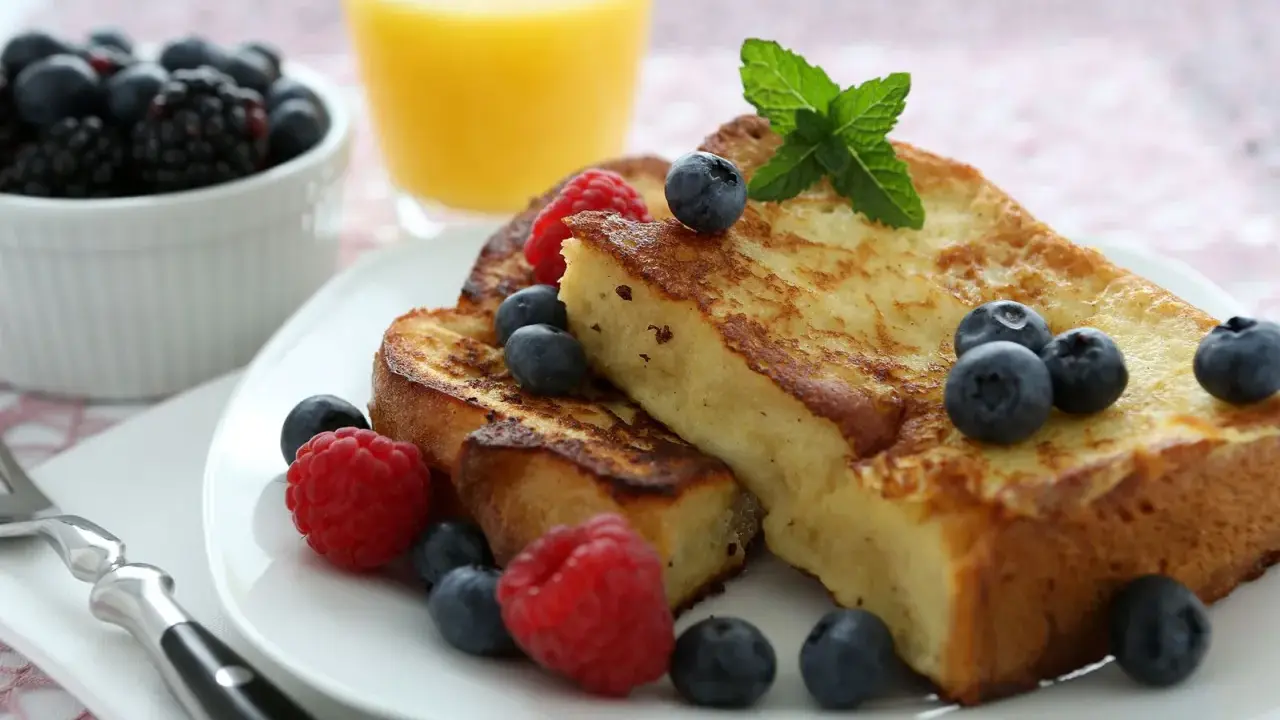 Deliciosa french toast receta, dorada y esponjosa, adornada con frambuesas, arándanos y menta. Un desayuno perfecto.