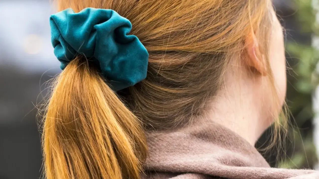 En hästsvans med en turkos scrunchie i sammet. Håret är kopparfärgat och faller mjukt.