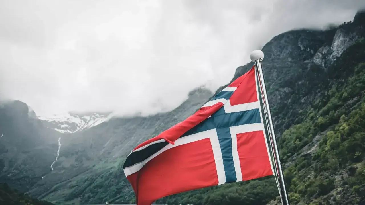 Norweska flaga na tle fiordu. Marzenie o pracy w Norwegii staje się rzeczywistością.