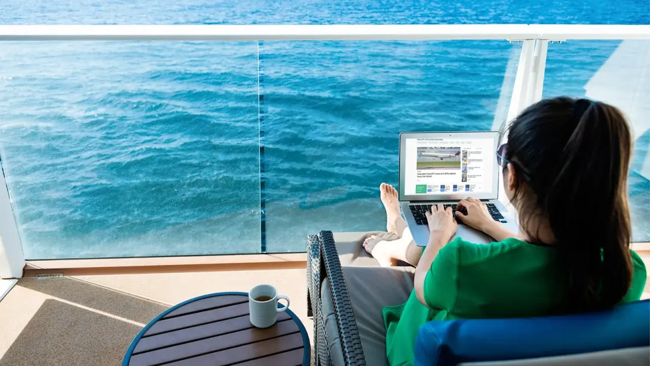 Donna su balcone di nave MSC lavora al laptop, con mare blu sullo sfondo. Scopri il pacchetto WiFi MSC e il suo costo per restare sempre connesso.
