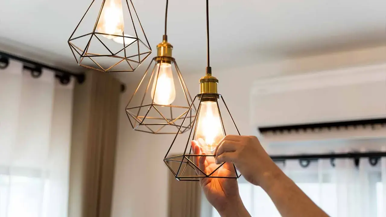 Man changing a lightbulb in a modern geometric pendant lamp, part of the simple home interiors.