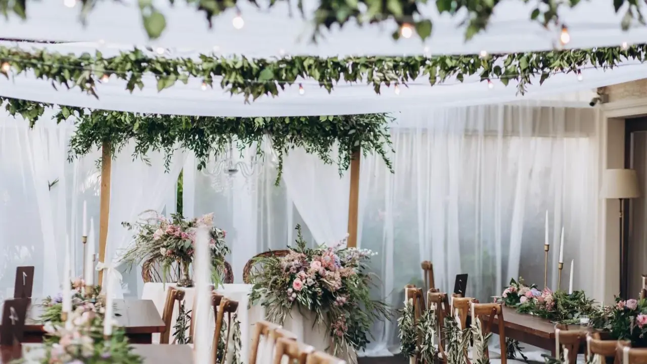 Uroczysty stół weselny w stylu boho, udekorowany kwiatami, zielenią i świecami.
