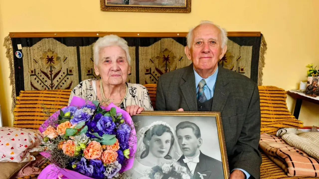 Para świętuje 70 rocznicę ślubu, trzymając zdjęcie z dnia zaślubin. W bukiecie kwiatów dominują fiolety i pomarańcze.