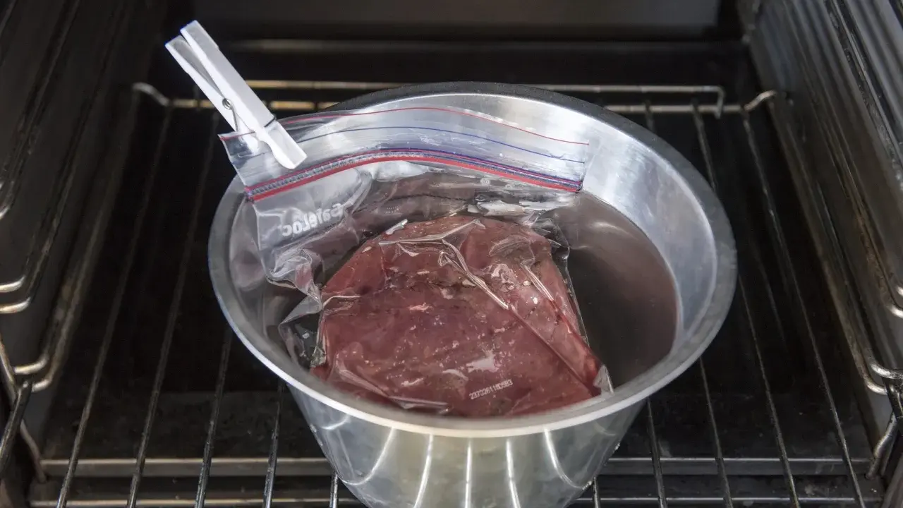 Vildsvinskött i vakuumpåse i en skål med vatten, redo för sous vide. Kontrollerar innertemp för perfekt resultat.
