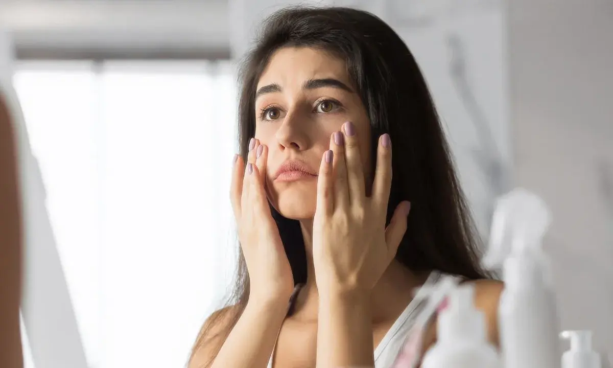 Donna preoccupata si tocca il viso, notando i segni dello stress sulla pelle.