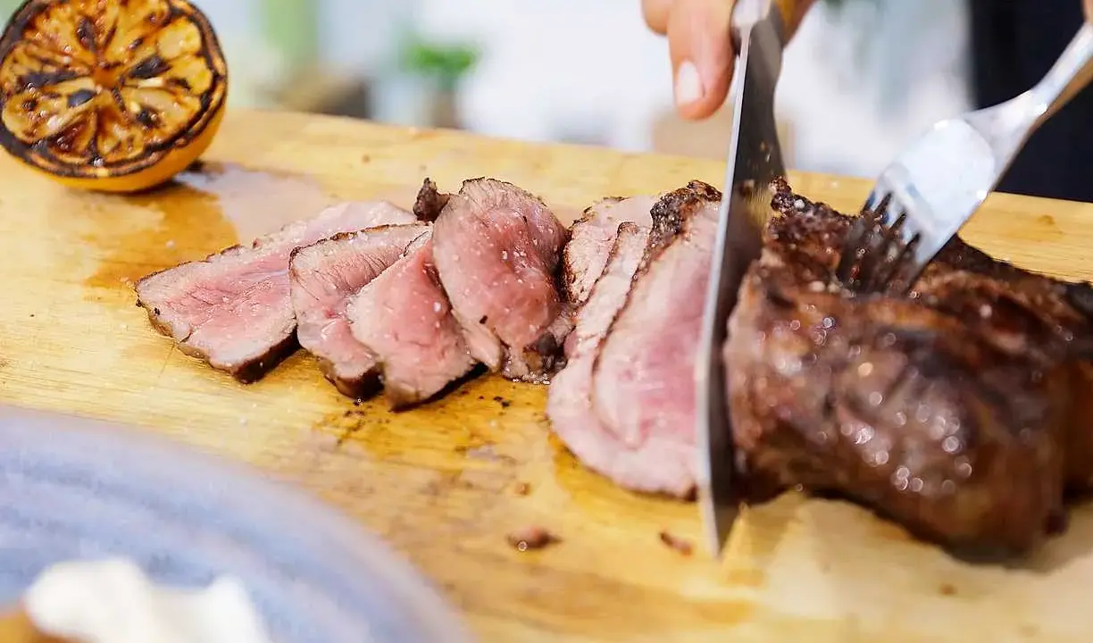 Perfekt grillad ryggbiff skärs upp på en skärbräda. Bredvid ligger en grillad citronhalva.