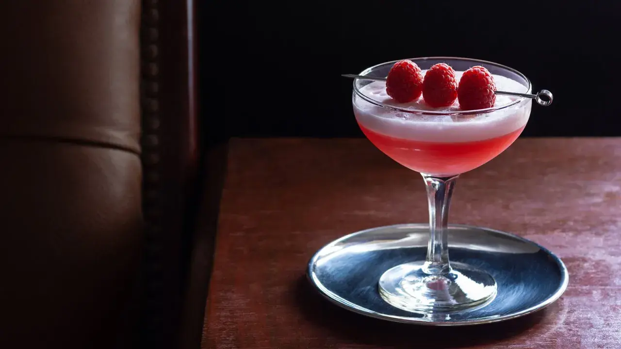 Ein eleganter Clover Club Cocktail mit Himbeeren auf einem silbernen Untersetzer, bereit zum Genuss.
