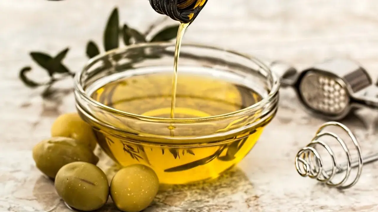 Aceite de oliva vertiéndose en un cuenco, con aceitunas y un pasapurés. ¡Cuidado! el aceite se pone malo si no se conserva bien.