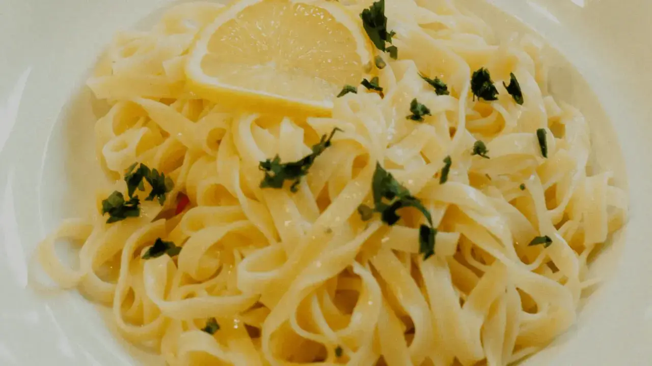 En tallrik med krämig citronpasta, toppad med en citronskiva och färsk persilja. Perfekt för en lätt lunch eller middag.