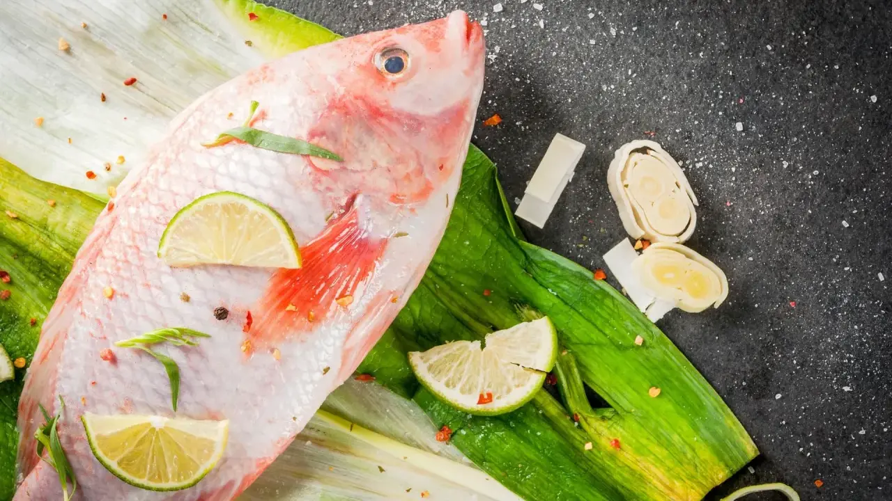 Cała ryba tilapia, przyprawiona chili i limonką, leży na zielonych liściach. Czy to tilapia, co to za ryba?